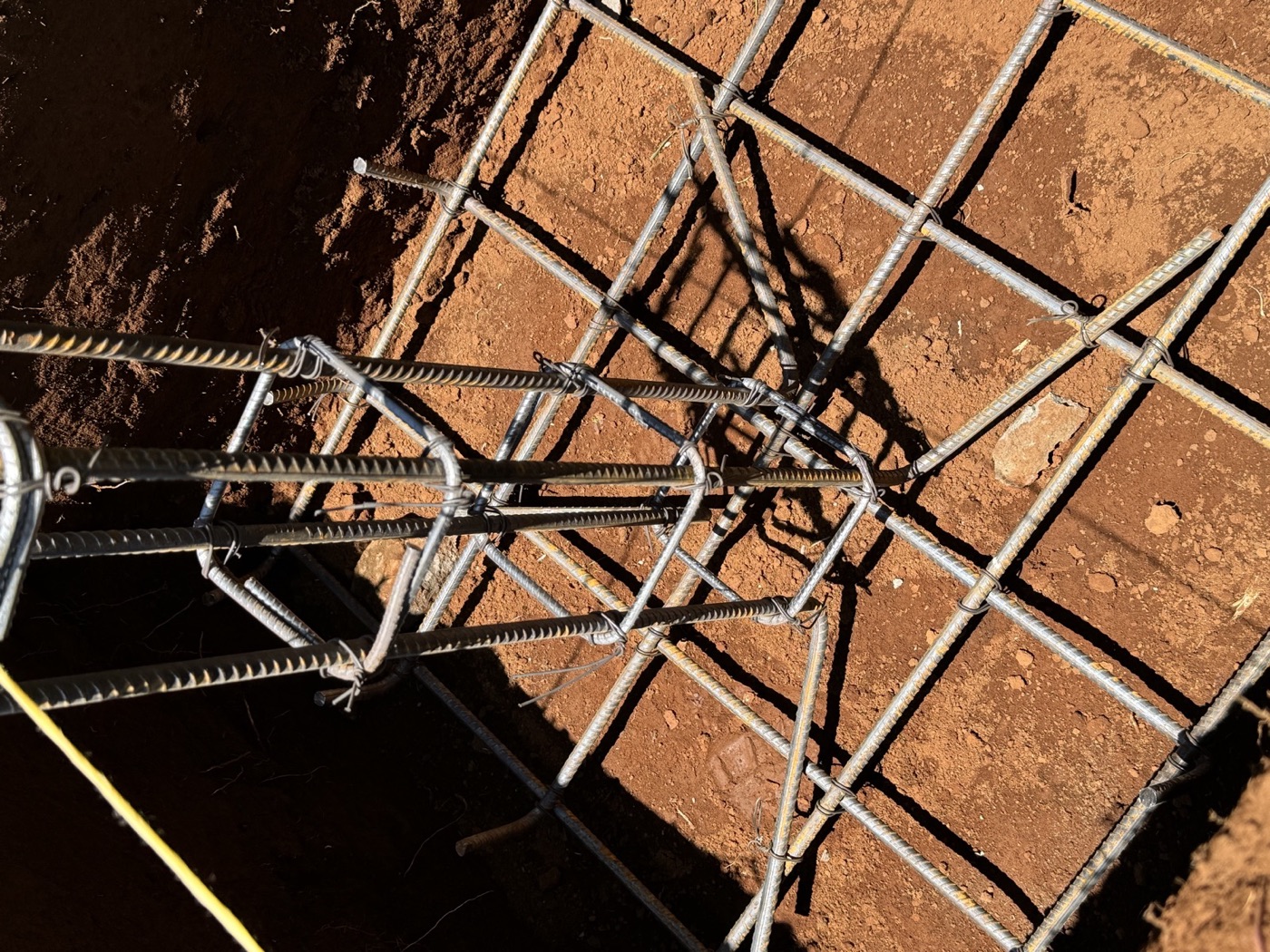 Bent column starter bars and square stirrups tied above a pad footing mat of crossing reinforcement bars inside an excavation
